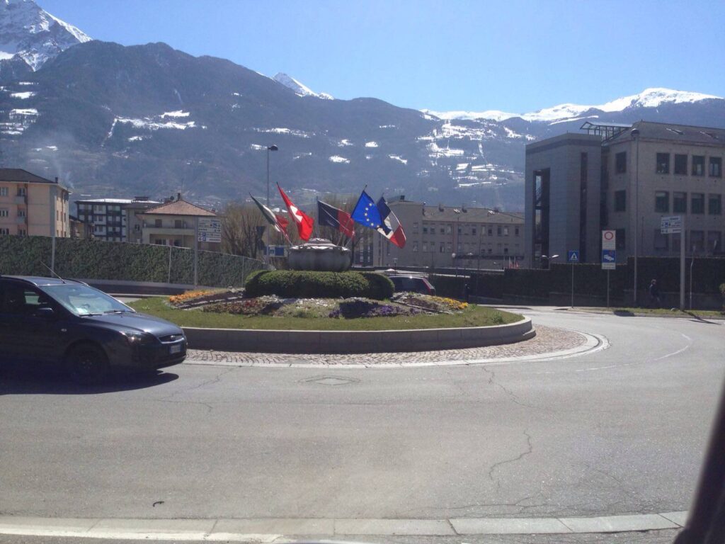 Rotonda stradale con cordoli in pietra naturale e panorama montano, Aosta.